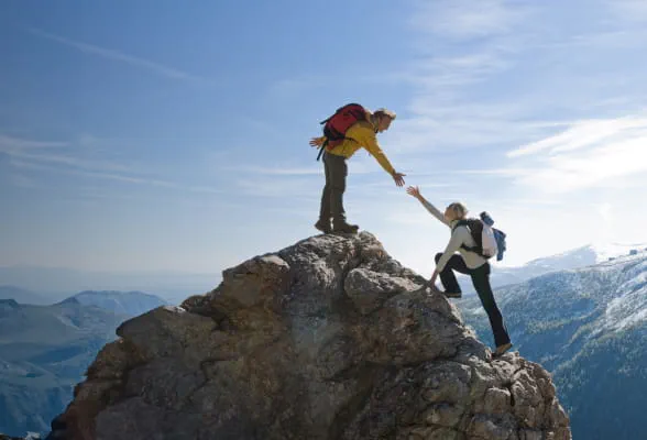 Two climbers helping each other on a mountain peak, symbolizing StoneX Wealth Management’s collaborative and supportive financial services for businesses