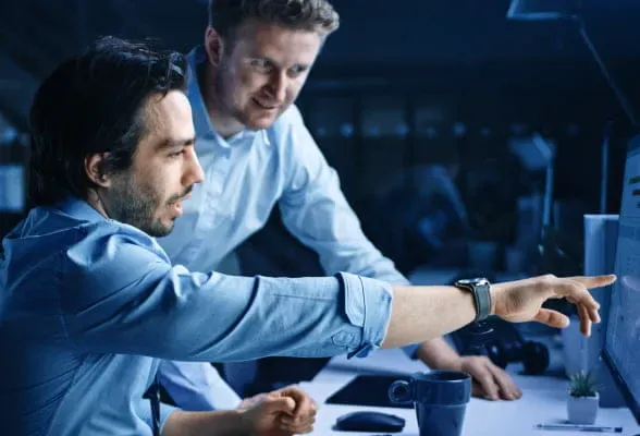Two professionals discussing data on a screen, representing StoneX Pro's turnkey FX solutions and expert guidance.