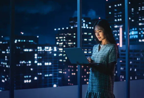Financial expert using StoneX Pro's platform, while holding the laptop, to analyze FX markets at night