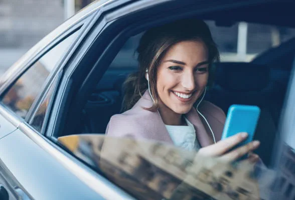 Woman smiling while using a smartphone in a car, reflecting StoneX Wealth Management's personalized financial solutions for private clients