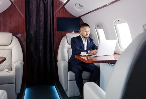 Professional working on a laptop in a private jet, illustrating StoneX Wealth Management's holistic support through the Wealth Solutions Group