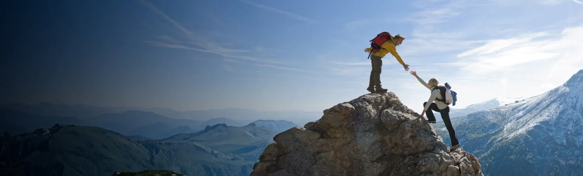 Two hikers assisting each other on a mountain, symbolizing StoneX Wealth Management's flexible affiliation options for financial professionals