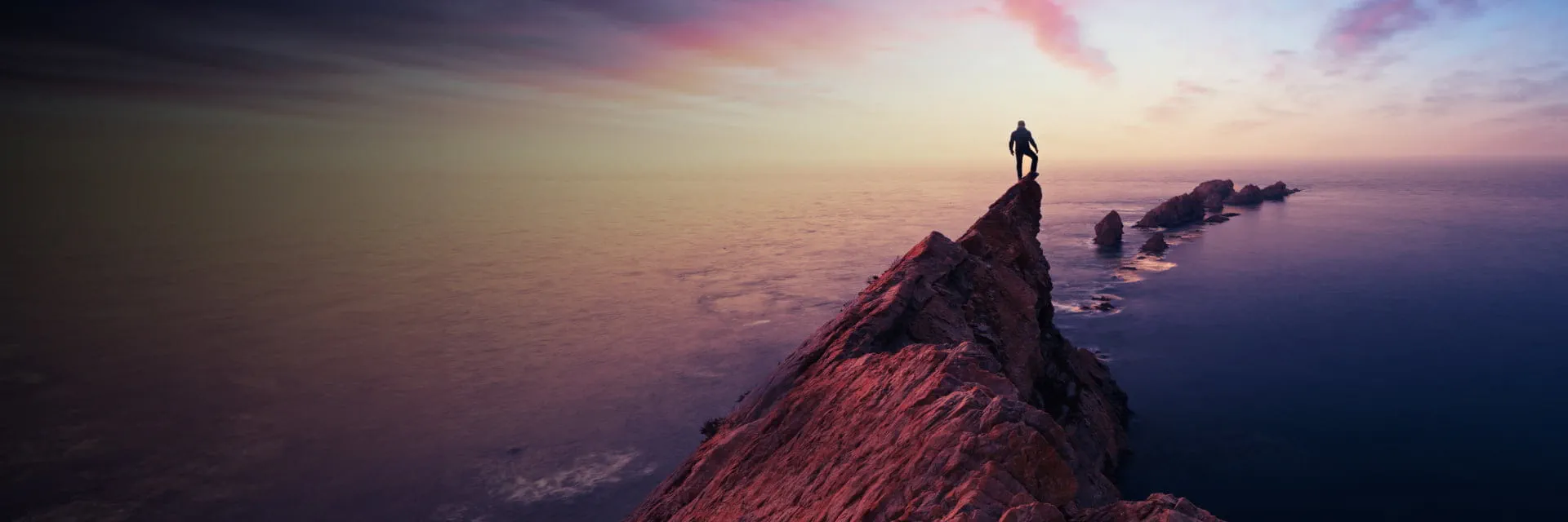 Person standing on a cliff at sunset, symbolizing StoneX Wealth Management's comprehensive solutions and support for financial professionals